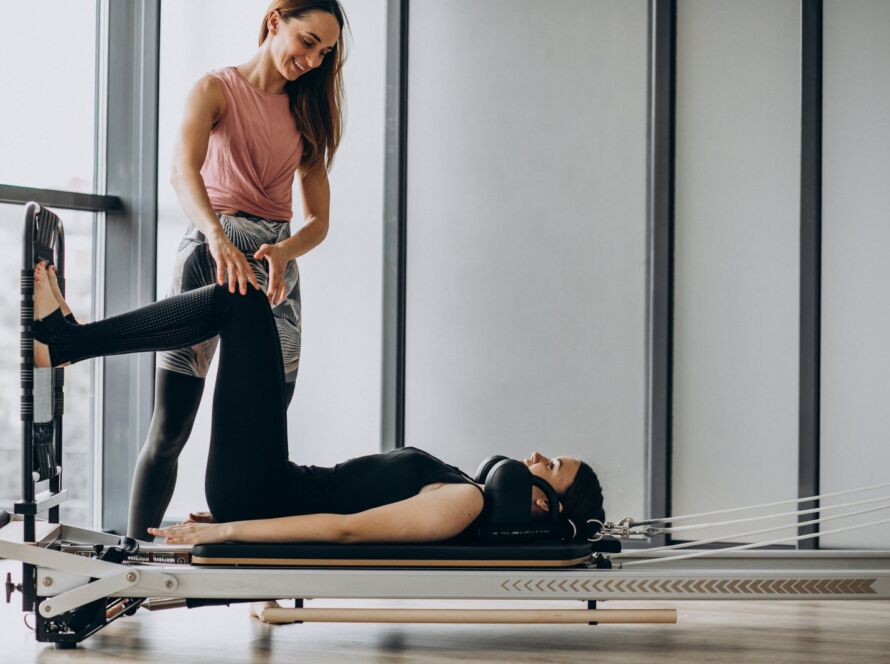 Birebir reformer pilates dersi: danışan reformer üzerinde sırtüstü çalışırken eğitmen bacağını yönlendiriyor